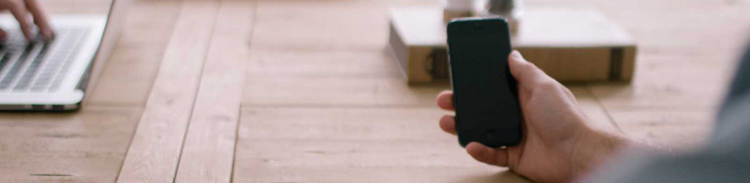 cropped-person-smartphone-office-table1.jpeg